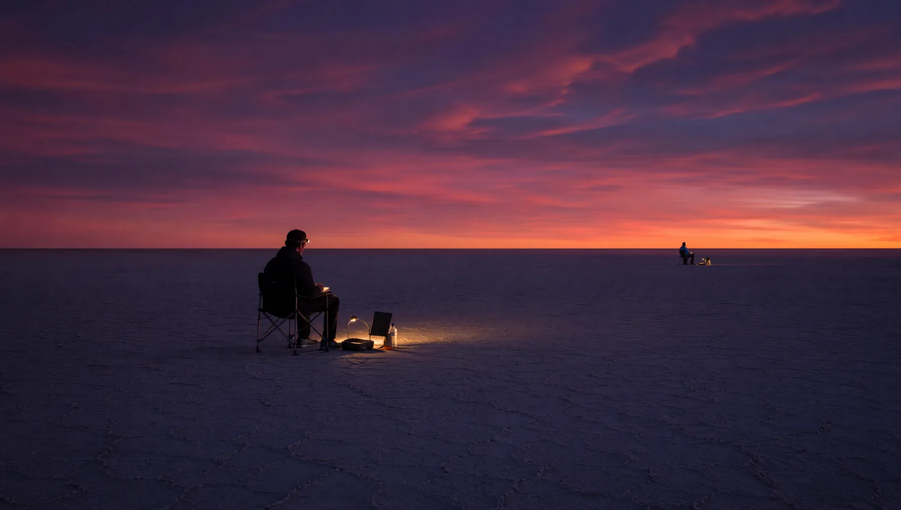 Two observers working independently across a vast salt-flat horizon at dusk