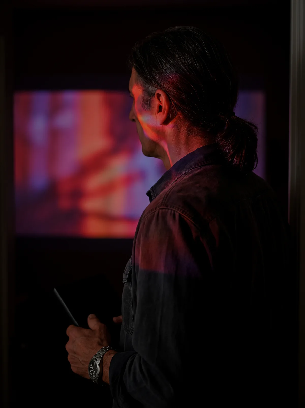Underexposed candid photograph of Silas Rain looking across a projection-lit room
